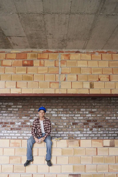 Trabajador de construcción sentado en la pared de ladrillo — Foto de Stock