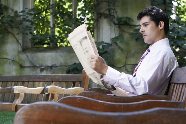 Businessman on bench reading newspaper — Stock Photo, Image