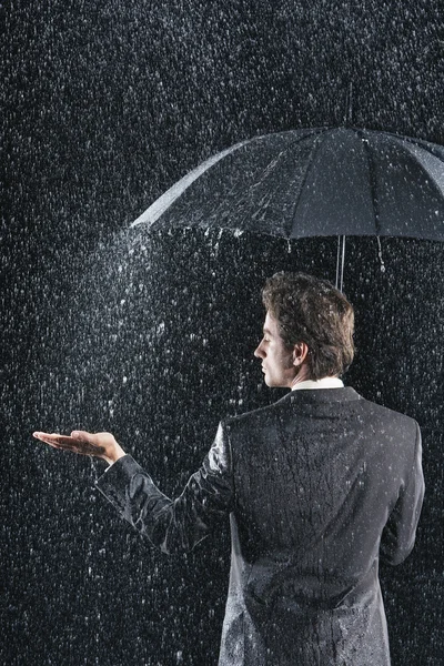Businessman sticking hand out from under umbrella — Stock Photo, Image