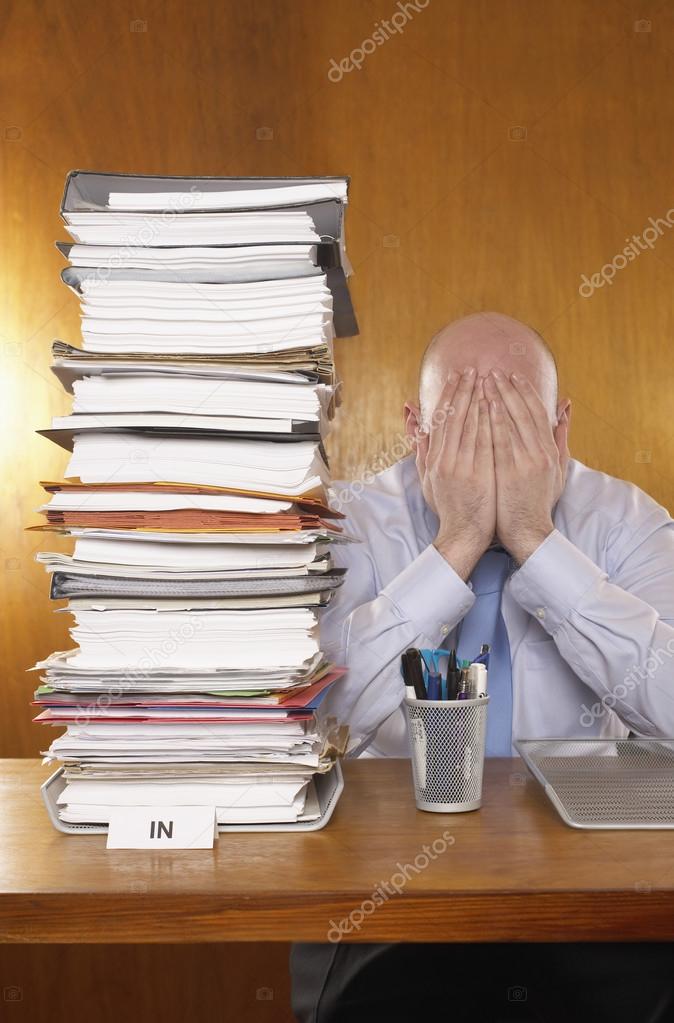 Businessman covering face next to stack of paper