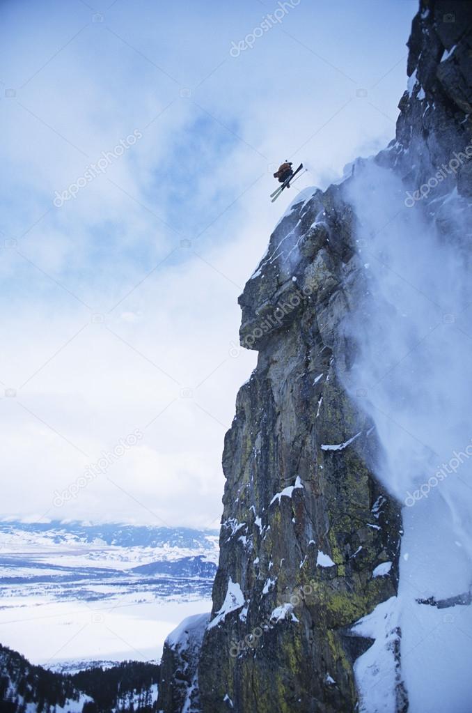 Skier jumping from cliff in mountains