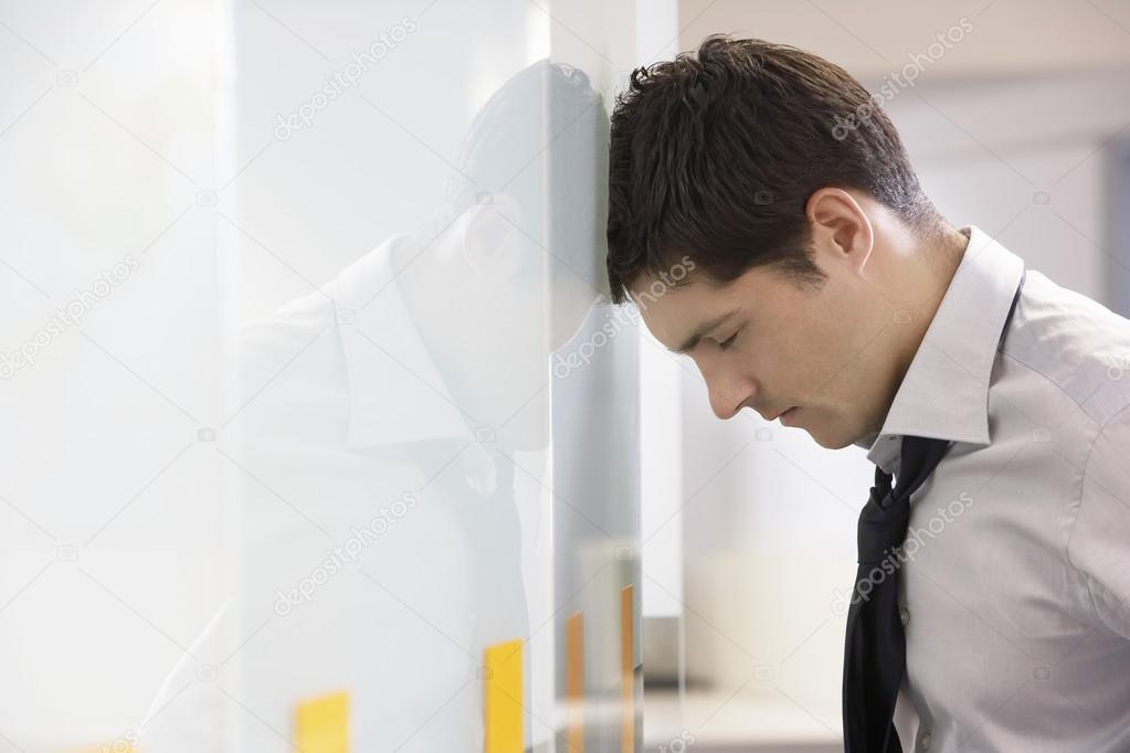 Unhappy Businessman resting head against wall