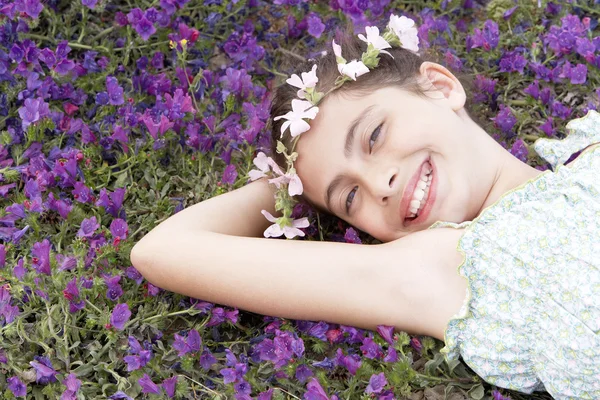 Flicka med blommor huvudbonad liggande i fältet — Stockfoto