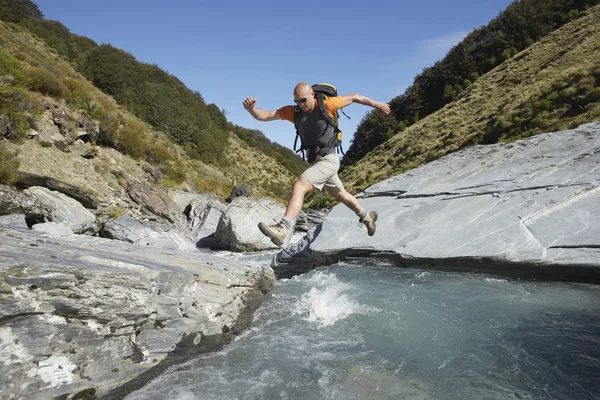 Hiker jumping across river — Stock Photo, Image