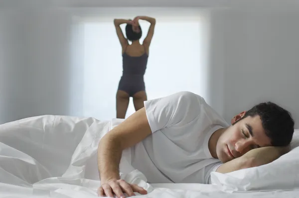 Man lying in bed and woman standing by window — Stock Photo, Image