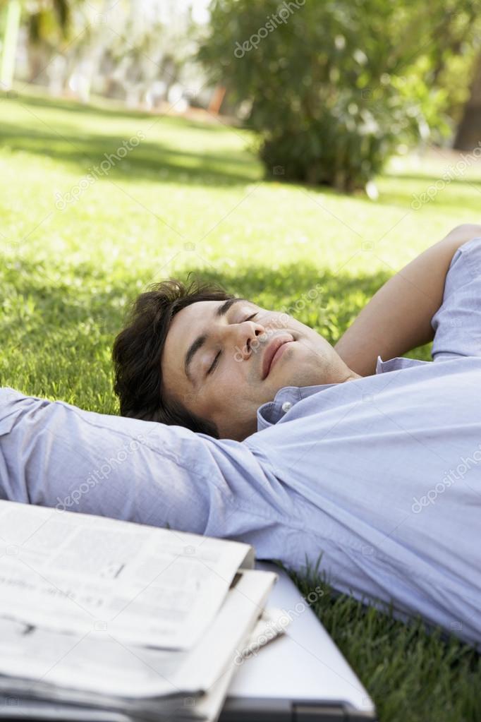 Mid-adult man lying on grass by newspaper close-up