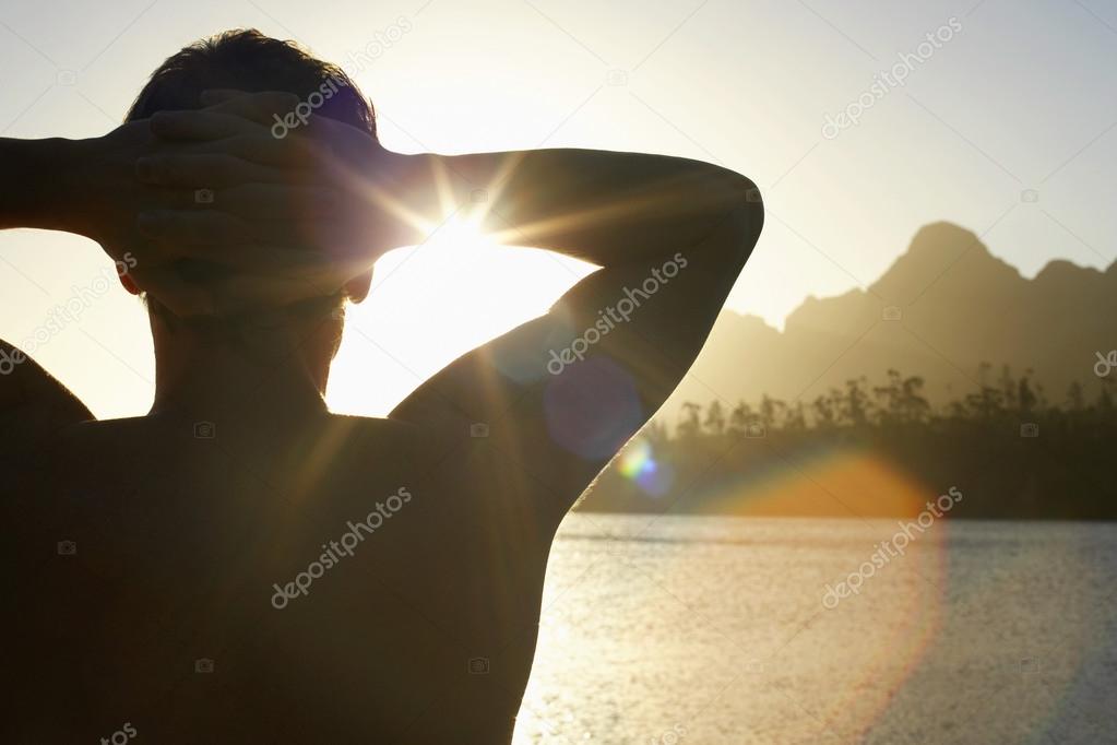 Man by lake with hands behind head