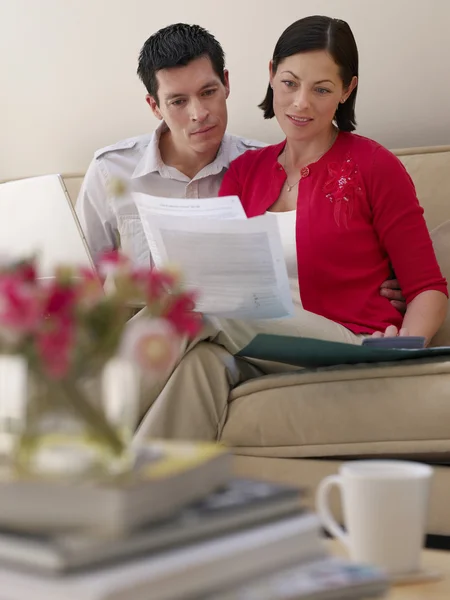 Couple using laptop and holding documents — Stock Photo, Image