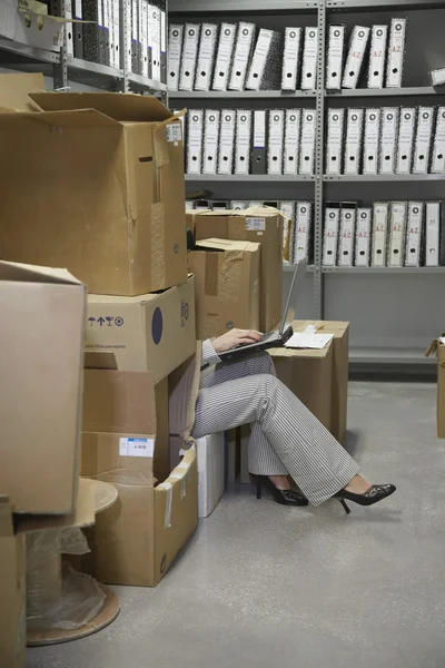 Woman using laptop in storage room — Stock Photo, Image