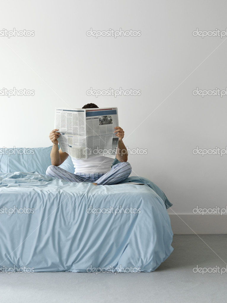 Man on bed reading newspaper