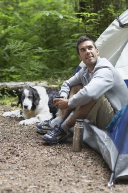 Çadır tarafından oturan köpekli adam