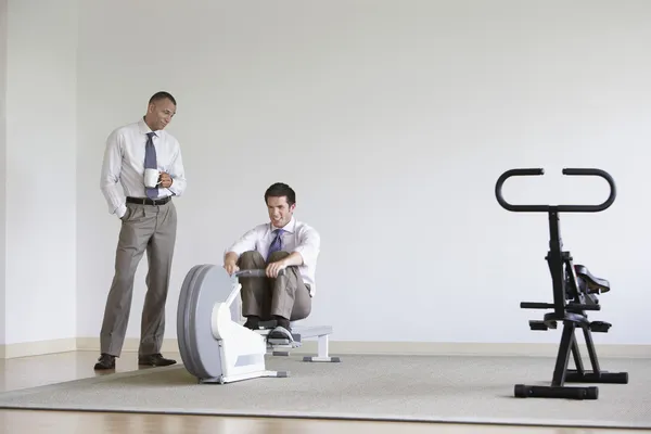 Businessman using rowing machine with colleague — Stock Photo, Image