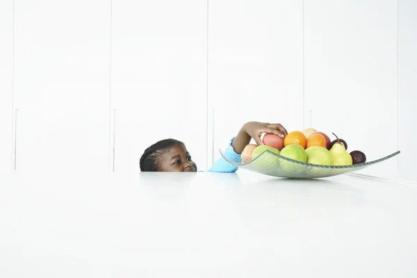 Chica alcanzando para la fruta en el tazón — Foto de Stock