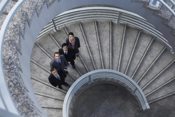 Four business associates standing on spiral staircase — Stock Photo, Image