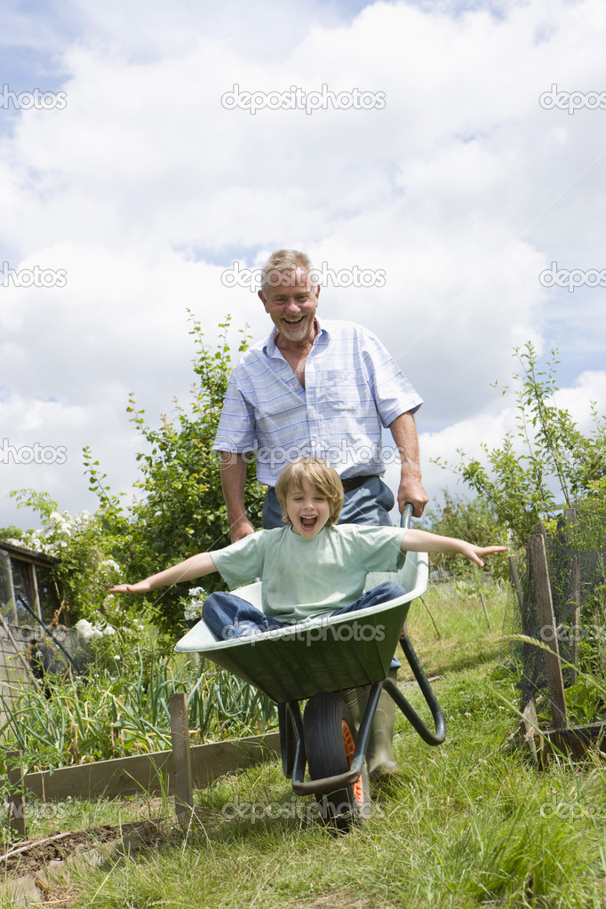 Grandfather pushing boy in wheel barrow