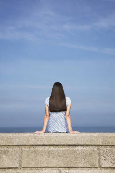 Young woman sitting on stone ledge — Stock Photo, Image