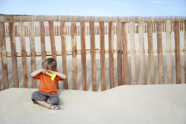 Boy sitting against wooden fence — Stock Photo, Image