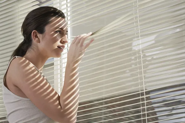 Vrouw gluren door blinds — Stockfoto