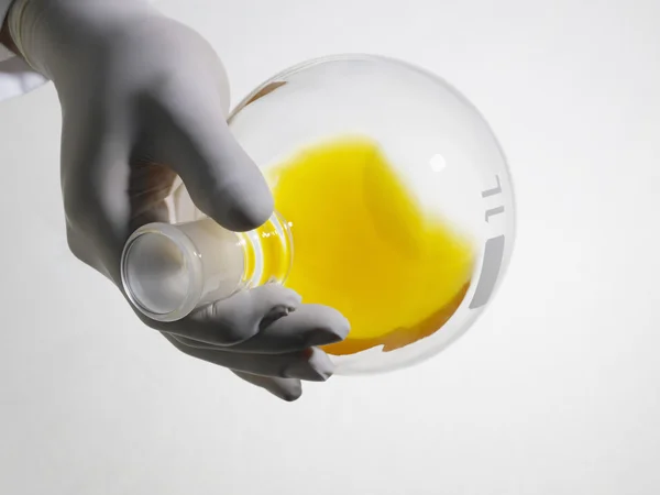 Человек, смешивающий желтую жидкость в лабораторной фляжке — стоковое фото