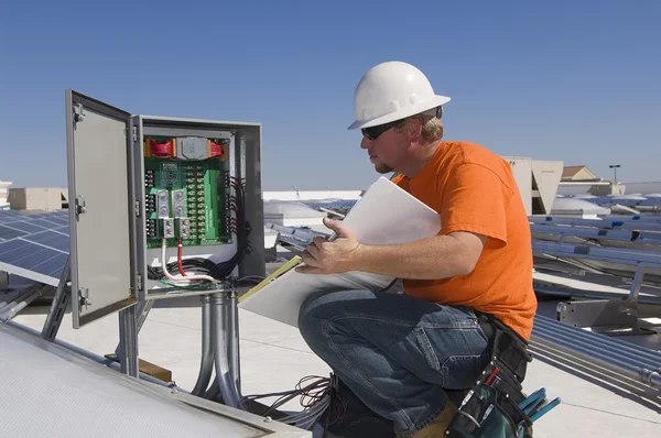 Electrical engineer writing notes while analyzing electricity box — Stock Photo, Image