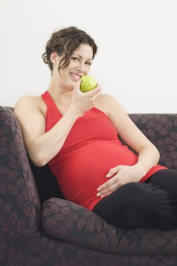 Kadın kanepede elma yiyor.