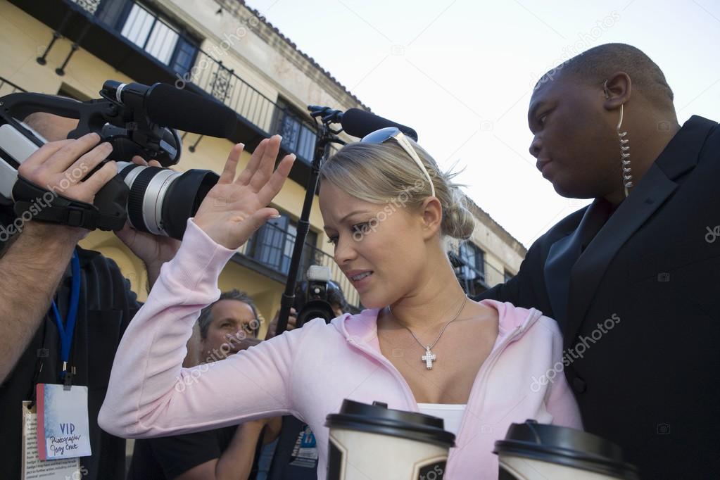 Female celebrity with bodyguard and paparazzi