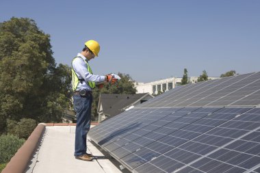 Maintenance worker stands with solar array on rooftop clipart