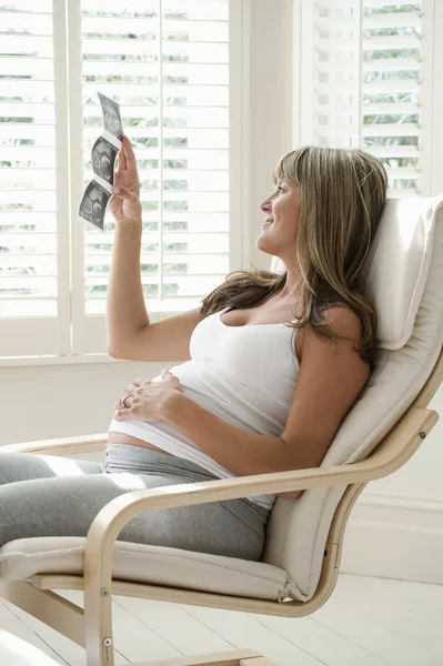 妊娠中の女性は赤ちゃんのスキャン写真で椅子に座って — ストック写真