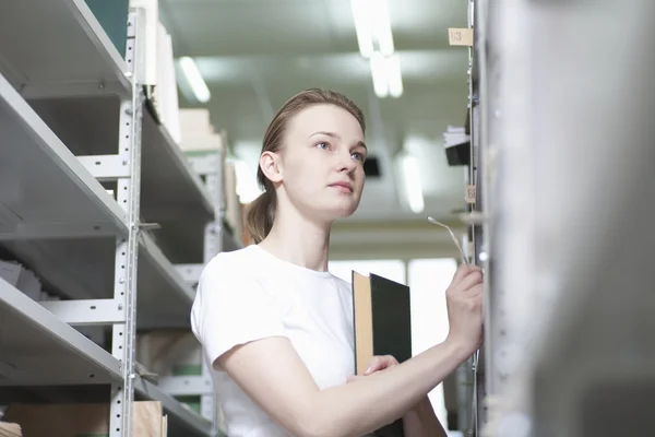 Jonge vrouw staat op bibliotheek rekken — Stockfoto