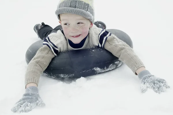 Ragazzo in abbigliamento invernale slittino su uno pneumatico interno — Foto Stock