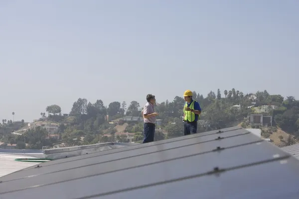 Работники техобслуживания стоят с солнечными батареями на крыше — стоковое фото