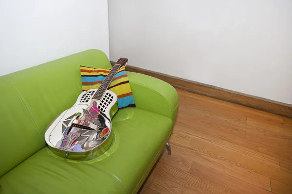 Resofonickou kytaru na zelené sofa — Stock fotografie