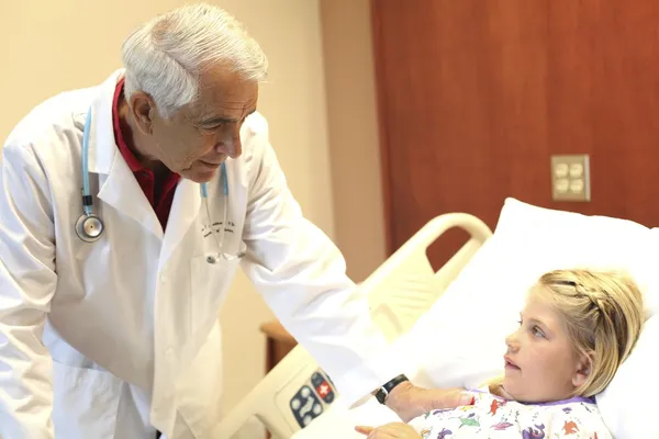 Médico idoso se inclina sobre paciente em pediatria — Fotografia de Stock