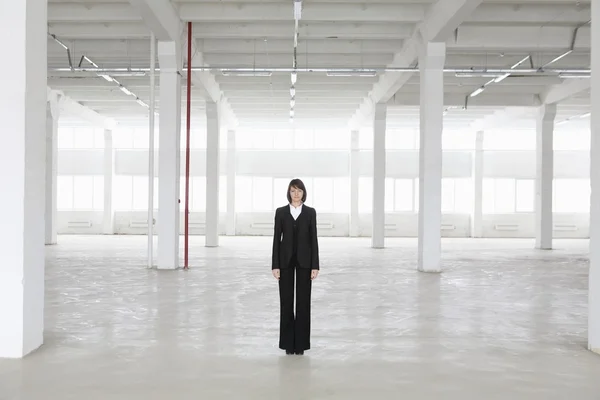 Business woman stands in empty warehouse — Stock Photo, Image