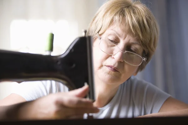 Mature woman adjusts foot of sewing machine — Stock Photo, Image