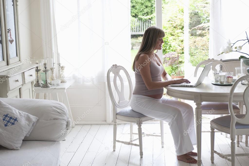 Pregnant woman sitting at table using laptop