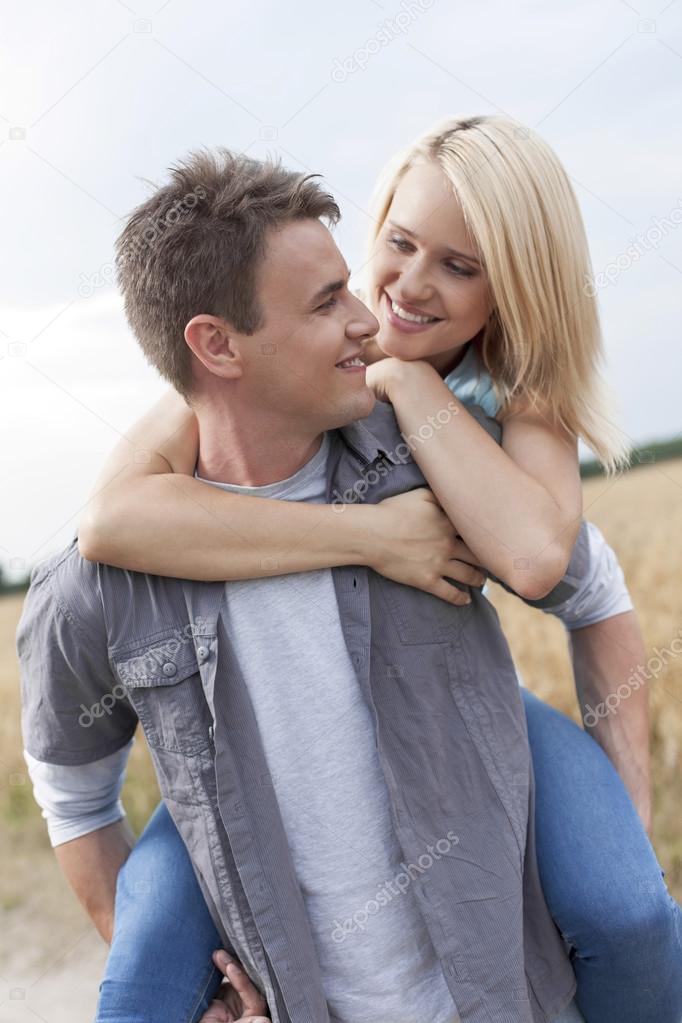 Man piggybacking woman on field