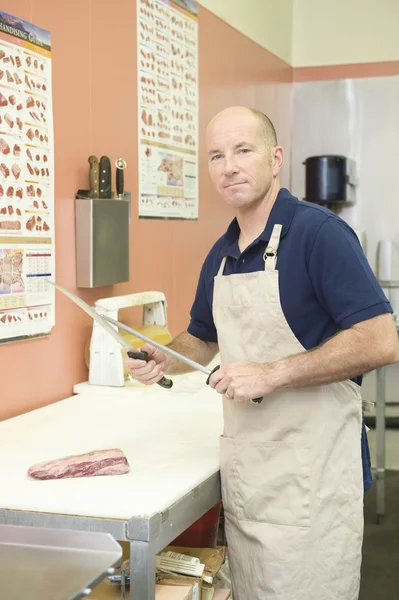 Supermarket employee sharpening knife at meat — Stock Photo, Image