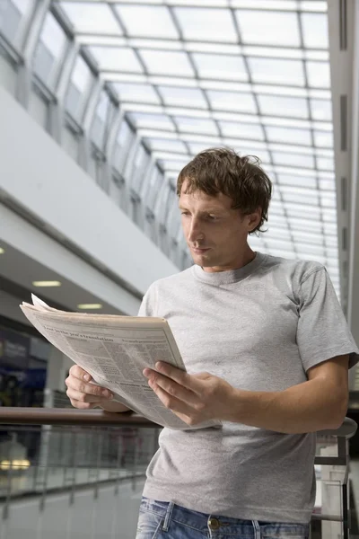 Young man stands reading newspaper — Stock Photo, Image