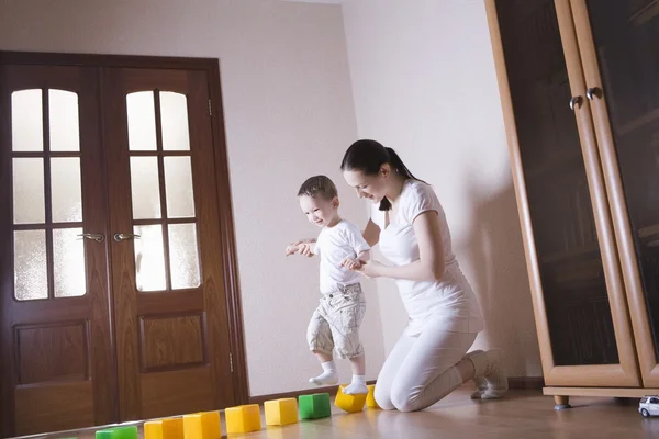 Boy walks along building blocks with help from his mother — Stock Photo, Image