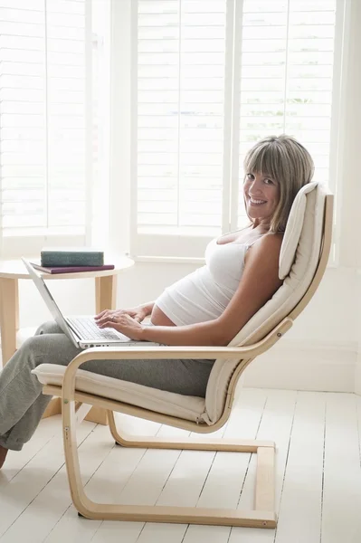 Schwangere sitzt mit Laptop auf Stuhl — Stockfoto