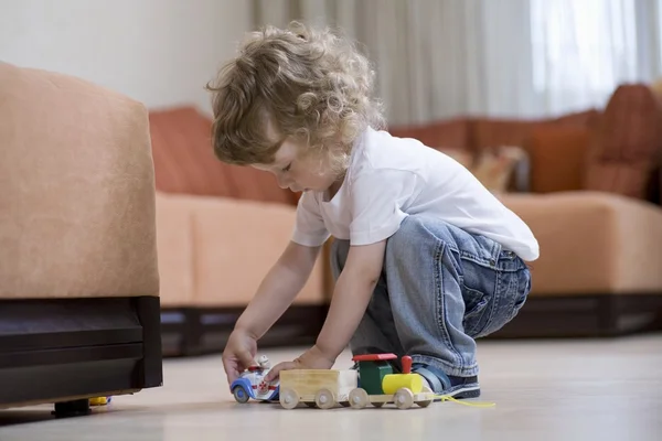 Blonde toddler playing with toy train on floor — Stock Photo, Image