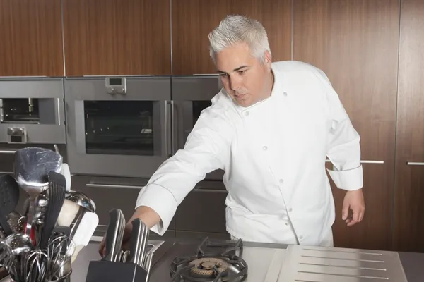 Mid adult chef leans for knife — Stock Photo, Image