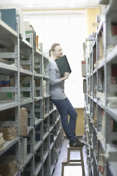 Vrouw staat op kruk in bibliotheek — Stockfoto