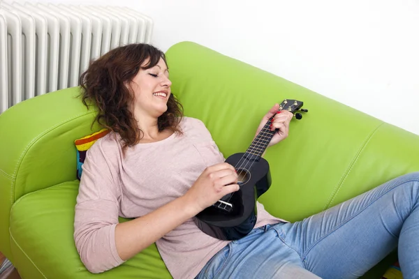 Žena na gauči hraje na ukulele — Stock fotografie