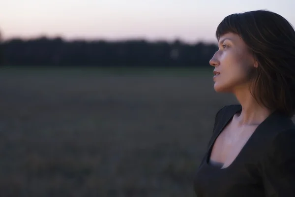 Frau steht in der Dämmerung auf einem Feld — Stockfoto