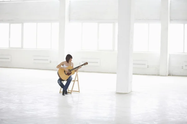 Donna seduta con chitarra acustica in magazzino vuoto — Foto Stock