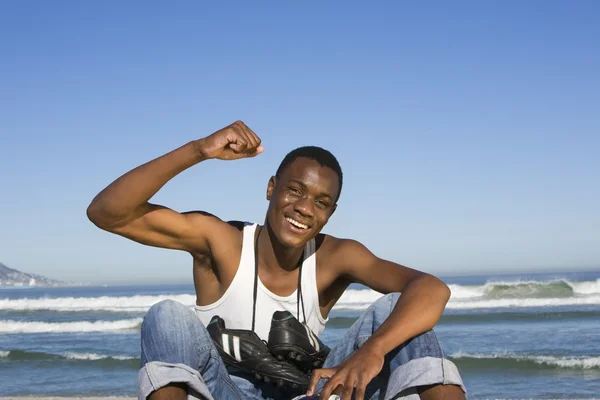 Мужчина, сидящий на пляже с футбольными сапогами на шее, аплодирует — стоковое фото