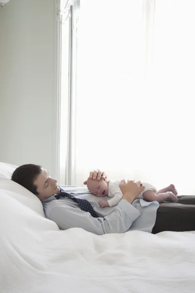 Working father lies with two week newborn on bed — Stock Photo, Image
