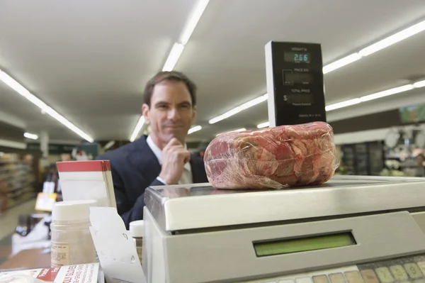 Man looks at selected meat on weighing machine — Stock Photo, Image